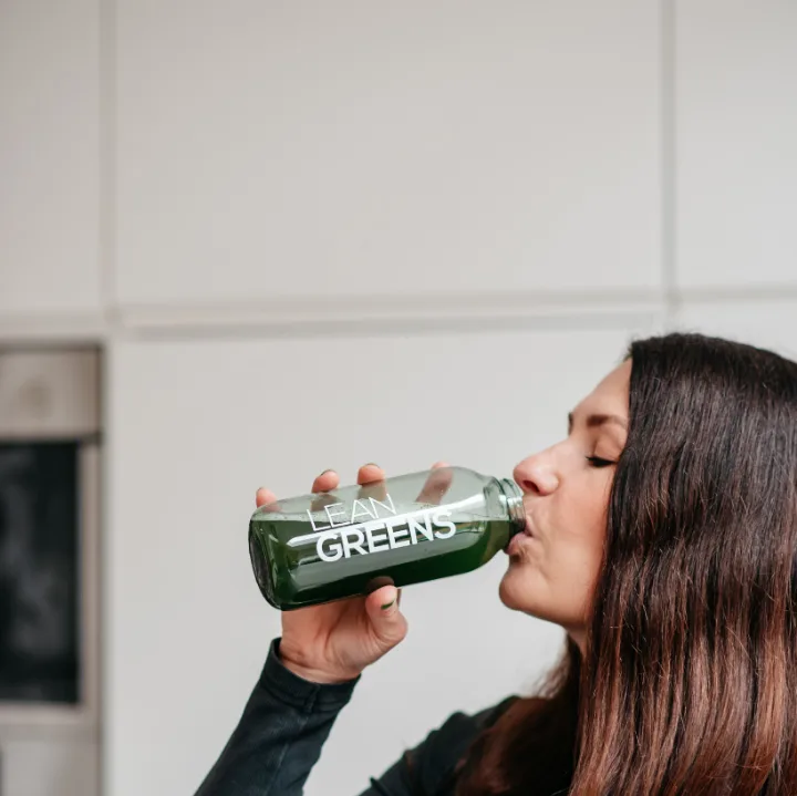 A woman drinking Collagen Greens from a bottle in her kitchen