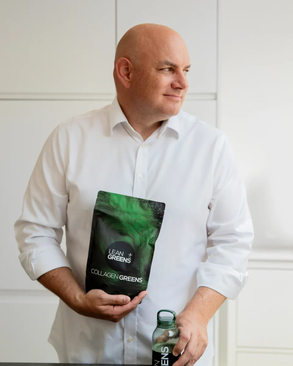 Tim, co-founder of Lean Greens, in his kitchen holding a pouch of Collagen Greens with a bottle of the drink on the counter